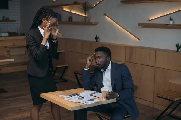 stressed african american businessman with colleague on meeting in cafe