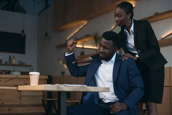 stressed african american businessman with colleague doing massage on meeting in cafe