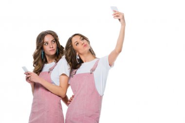 attractive young twins taking selfie with smartphone isolated on white clipart