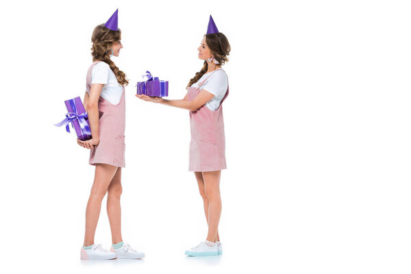 вид сбоку красивых маленьких близнецов, одаривающих друг друга подарками, изолированными на белом
