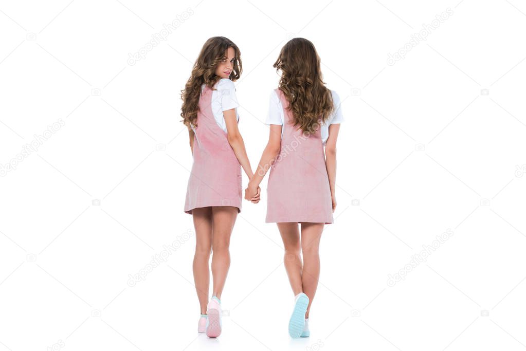 back view of young twins holding hands isolated on white