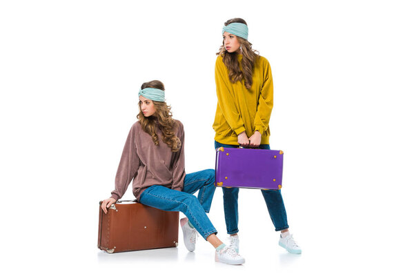 attractive retro styled twins with travel bags looking away isolated on white