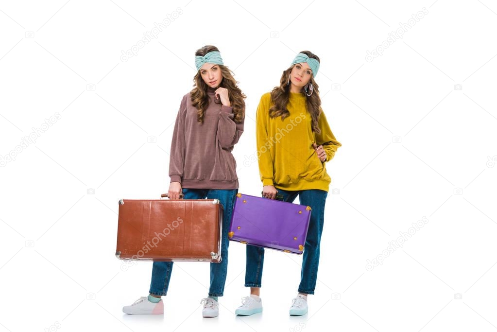 attractive retro styled twins standing with travel bags isolated on white