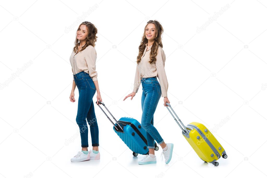 side view of happy young twins with wheeled bags isolated on white, travel concept