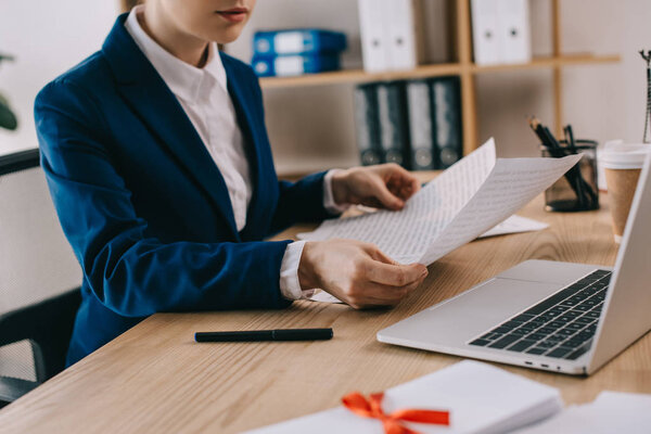 cropped shot of businesswoman doing paperwork at workplace with laptop in office