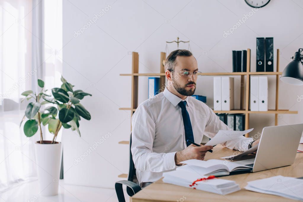 portrait of lawyer with documents sitting at workplace with laptop in office