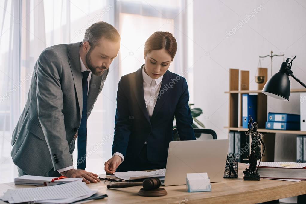 lawyers in suits working together on project at workplace with gavel and laptop in office