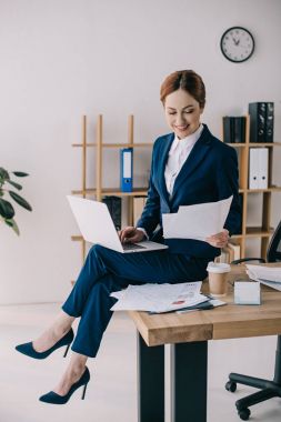 dizüstü bilgisayar ve belgeler Office masada oturan gülümseyen iş kadını