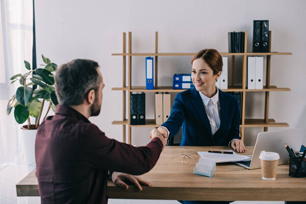 smiling businesswoman and client shaking hands on meeting in office