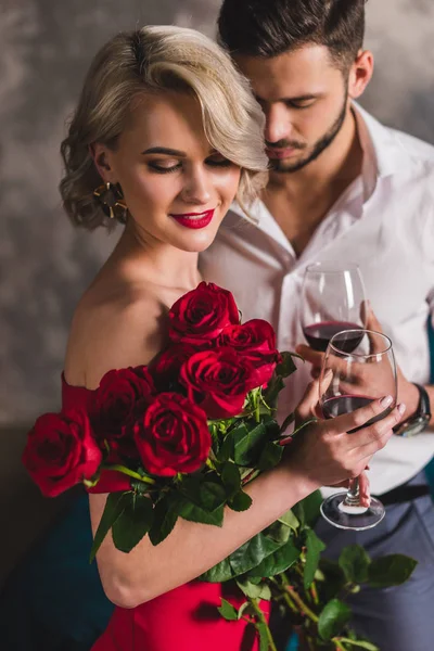 Улыбающаяся Молодая Женщина Красном Платье Держащая Красивые Розы Пьющая Вино — стоковое фото