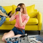 Giovane ragazza che scatta foto sulla macchina fotografica mentre imballava la borsa da viaggio a casa