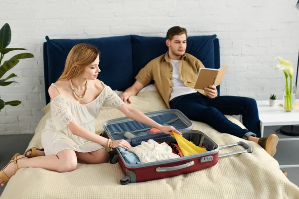 Pregnant Woman Packing Travel Bag Vacation While Husband Reading Book — Stock Photo, Image