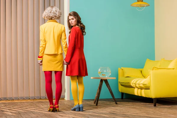 カラフルなアパート 人形の家のコンセプトで手を繋いでいる明るい色のレトロなスタイルの服の女性の背面図 — ストック写真