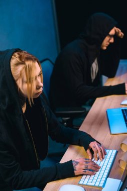 high angle view of serious female hacker working on new malware with accomplice  in dark room clipart