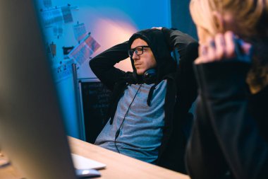 female hacker looking at depressed accomplice at workplace clipart