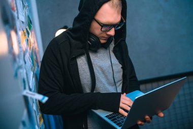 Kukuletalı hacker karanlık odada dizüstü bilgisayar ile kötü amaçlı yazılım geliştirme