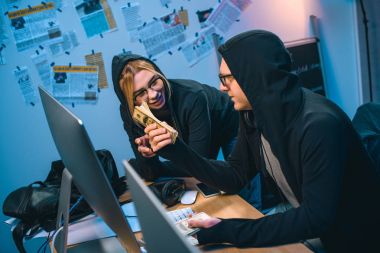 happy couple of hackers with stack of cash at workplace clipart