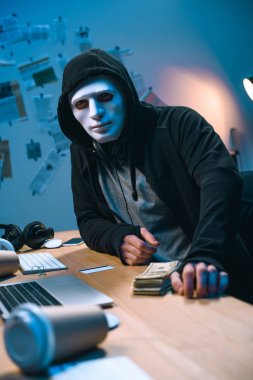 Masa üzerinde para yığını ile maskeli hacker