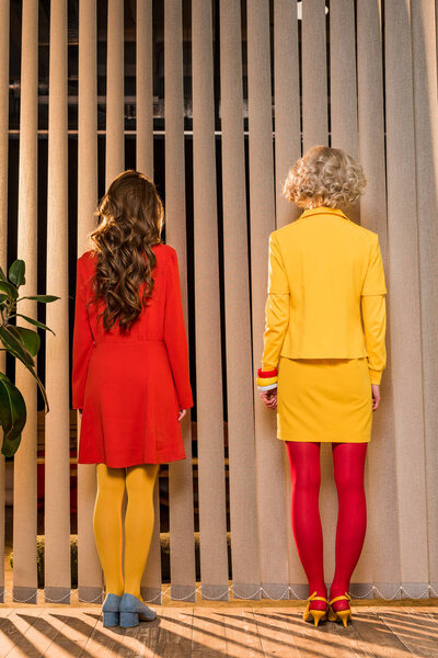 rear view of women in bright clothing standing at window at colorful apartment, doll house concept
