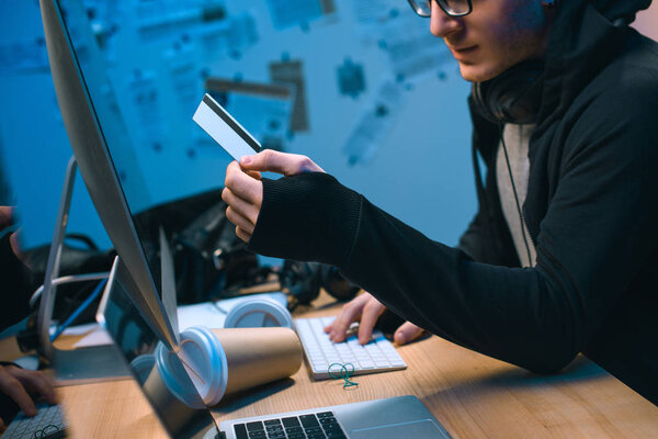 cropped shot of hacker holding stolen credit card in dark room