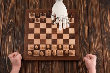 cropped shot of robot playing chess with human on wooden surface clipart