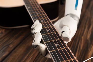 cropped shot of robot playing guitar over wooden surface clipart