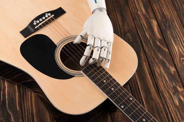 cropped shot of robot touching strings of acoustic guitar over wooden surface