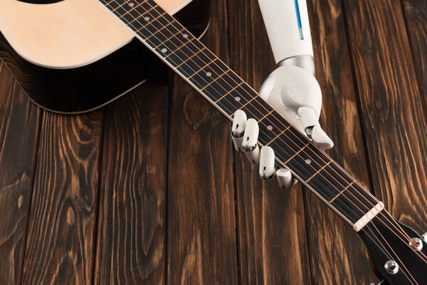 cropped shot of robot playing acoustic guitar over wooden surface