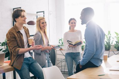 multicultural businesspeople with coffee and textbooks having meeting in modern office  clipart