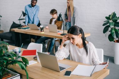 ders kitabı izlerken laptop ve arkasında modern ofis çalışma arkadaşları ile iş kadını 