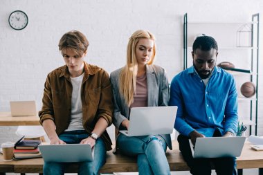 dizüstü bilgisayarlar kullanarak ve modern ofisindeki masada oturan üç çok kültürlü iş arkadaşları 