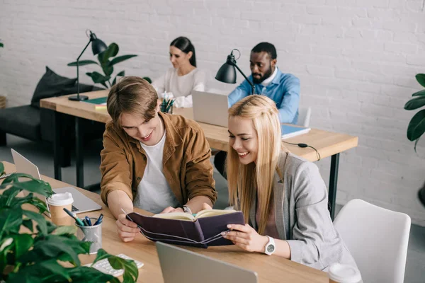 Sonrientes Socios Negocios Mirando Libro Texto Colegas Sentados Detrás Oficina — Foto de Stock