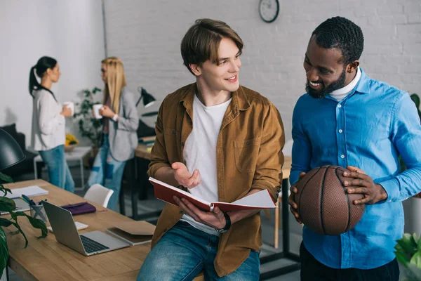 Hombre Negocios Afroamericano Sosteniendo Pelota Hablando Con Socio Con Libro — Foto de Stock