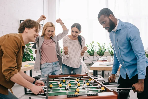 テーブル サッカーを祝うと女性の同僚を身振りで示すことの前で幸せな多文化ビジネスマンの側面図 — ストック写真