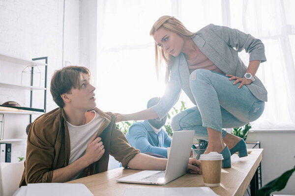 young businesswoman threatening and grabbing collar of colleague in modern office