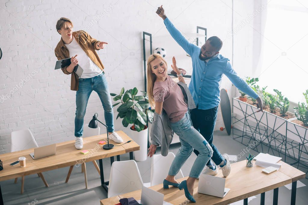high angle view of happy multiethnic business colleagues dancing and having fun in modern office 
