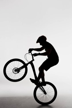 silhouette of trial biker standing on back wheel on white clipart