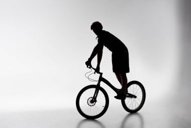 silhouette of trial cyclist in helmet balancing on bicycle on white clipart