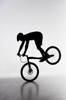 silhouette of trial biker performing front wheel stand on white clipart
