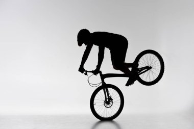 silhouette of trial cyclist performing front wheel stand on white clipart