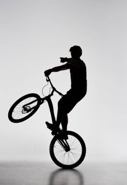 silhouette of trial biker standing on back wheel and pointing somewhere on white clipart