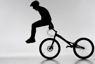 silhouette of trial biker performing stunt on bicycle on white clipart