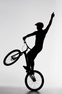 silhouette of trial cyclist standing on back wheel and raising hand on white clipart