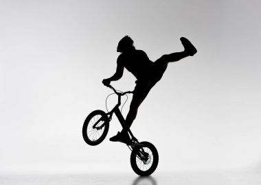 silhouette of trial biker performing stunt on bicycle on white clipart