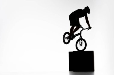silhouette of trial cyclist performing stunt while balancing on cube on white clipart