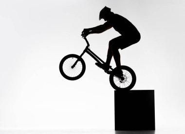 silhouette of trial cyclist performing back wheel stand while balancing on cube on white clipart