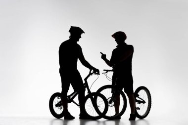 silhouettes of trial bikers with bicycles chatting on white clipart