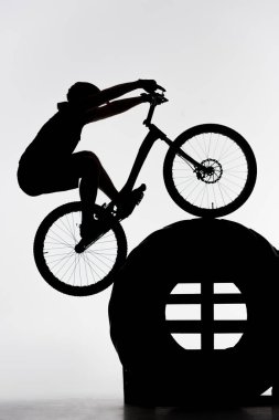 silhouette of trial biker balancing on tractor wheel on white clipart