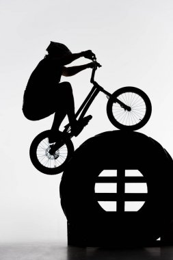 silhouette of trial biker jumping on tractor wheel on white clipart