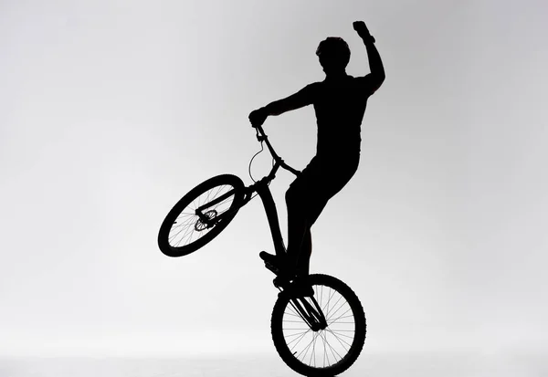 Silhouette Trial Biker Standing Back Wheel Raising Hand White — Free Stock Photo